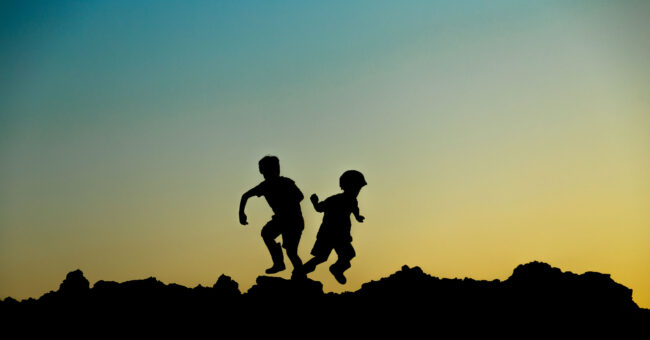 Zwei Kinder, die hüpfend auf einem Felsen spielen